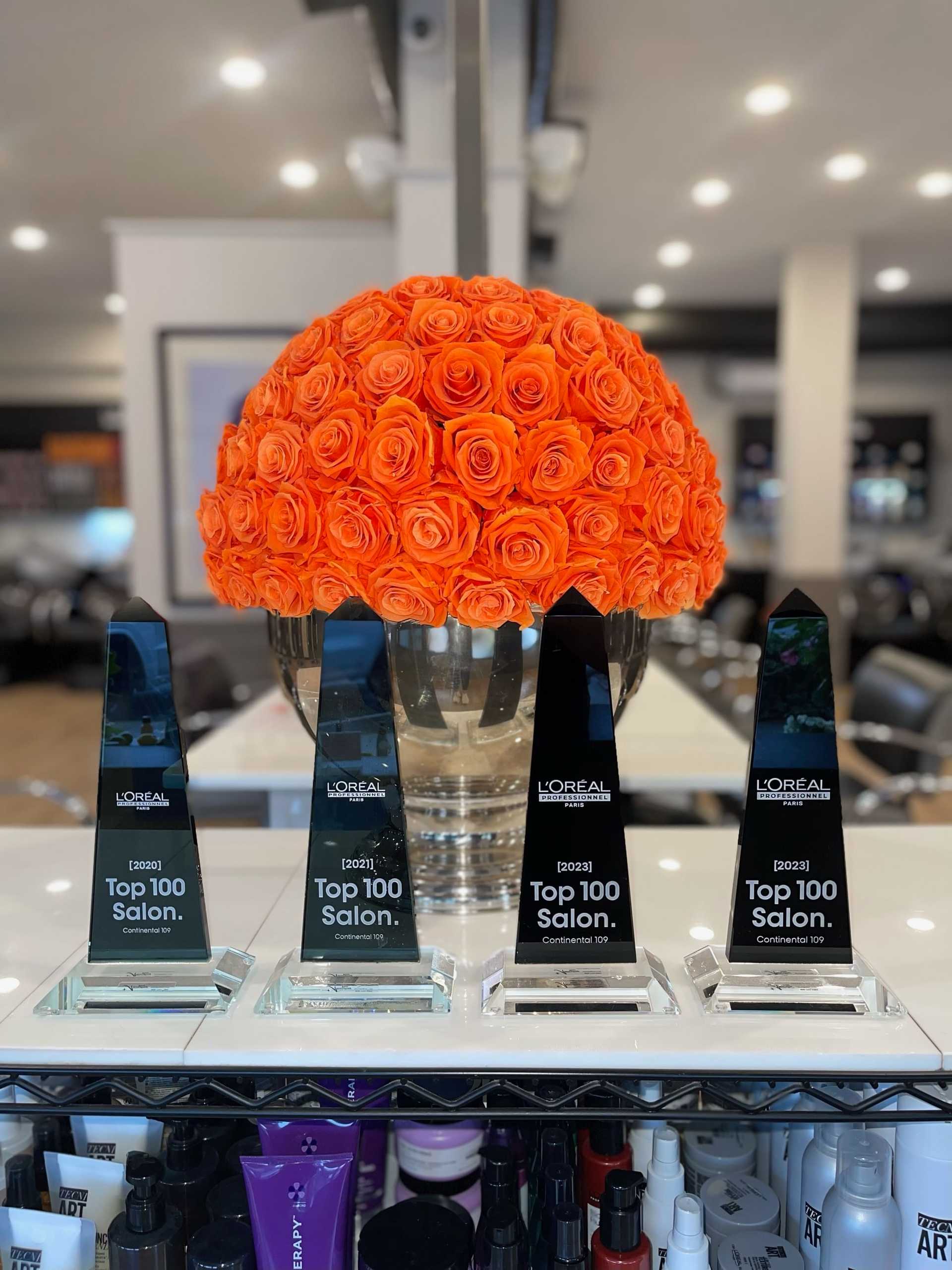 Four "Top 100 Salon" awards displayed in front of a vase of vibrant orange roses.