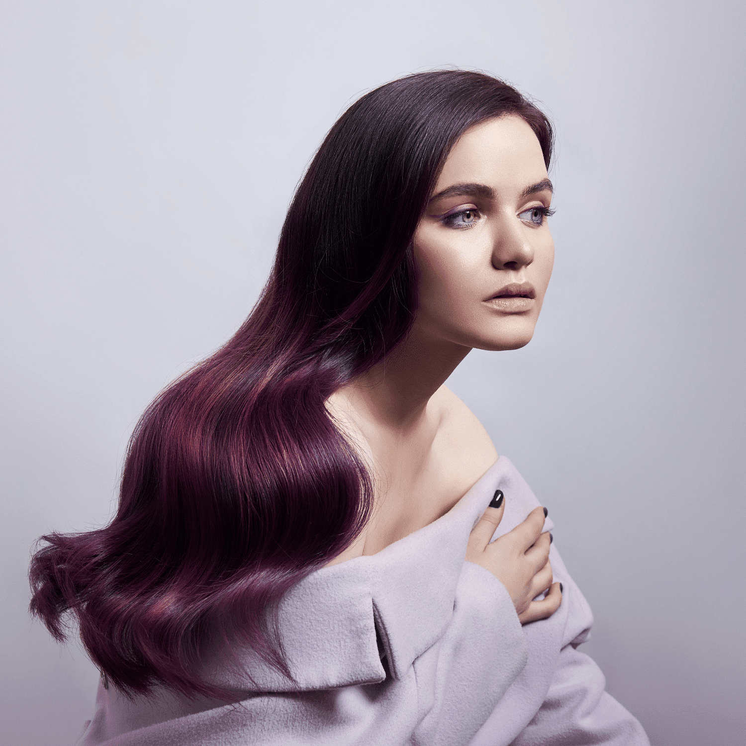 Woman with long, flowing purple-tinted hair in an off-shoulder lavender top, gazing thoughtfully.